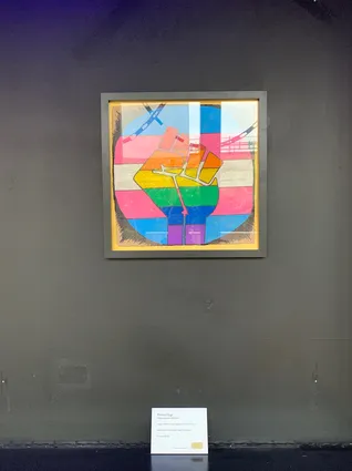 a framed placard with a blue pink and white background and a rainbow fist