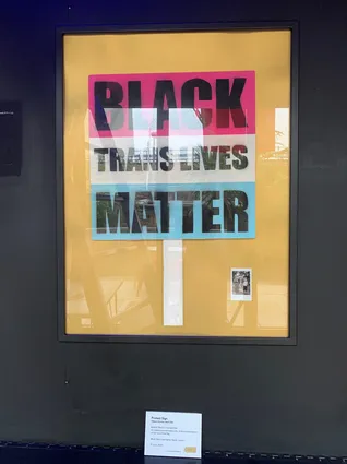 a framed placard that reads 'black trans lives matter' on a black wall
