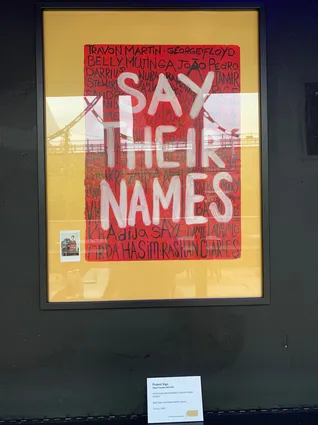 a framed placard that reads 'say their names' on a black wall