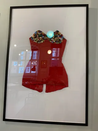 A framed red dress with a collar made of multicoloured buttons, the frame is black with a white background