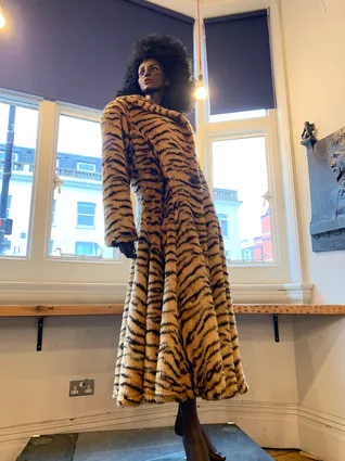 a black mannequin with curly hair wearing an ankle length tiger print fur coat