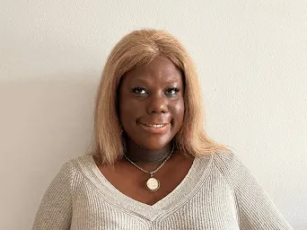 A portrait of a black woman with blonde hair wearing a light coloured top.
