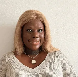 A portrait of a black woman with blonde hair wearing a light coloured top.