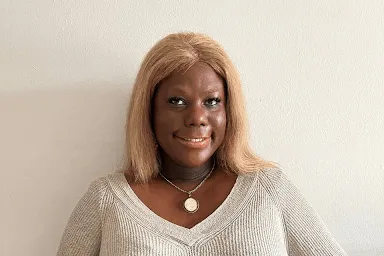A portrait of a black woman with blonde hair wearing a light coloured top.