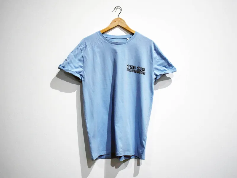 A blue t-shirt hanging on a coathanger, text on short reads 'The Tin Wardrobe'