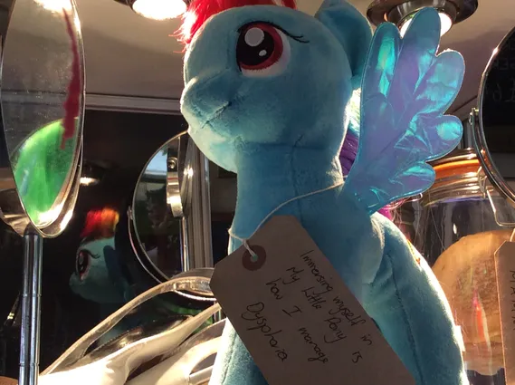 A stuffed toy of rainbow dash from my little pony, the toy has a brown tag tied around its neck