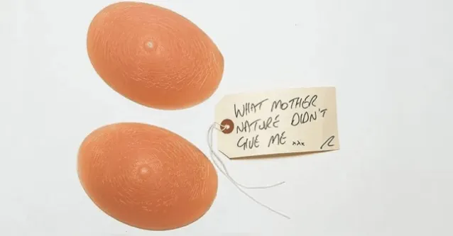 A pair of prosthetic breasts with a brown tag that reads 'what mother nature didn't give me xxx'