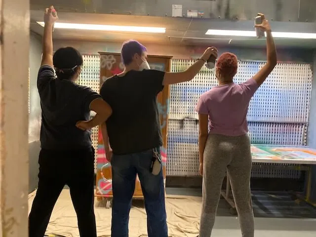 The back of three young people holding spray cans with their arms in the air