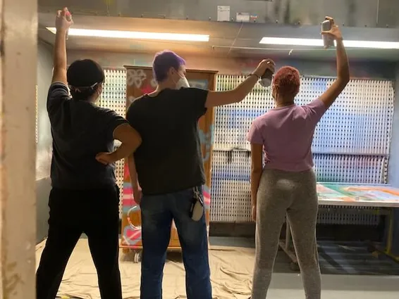 The back of three young people holding spray cans with their arms in the air