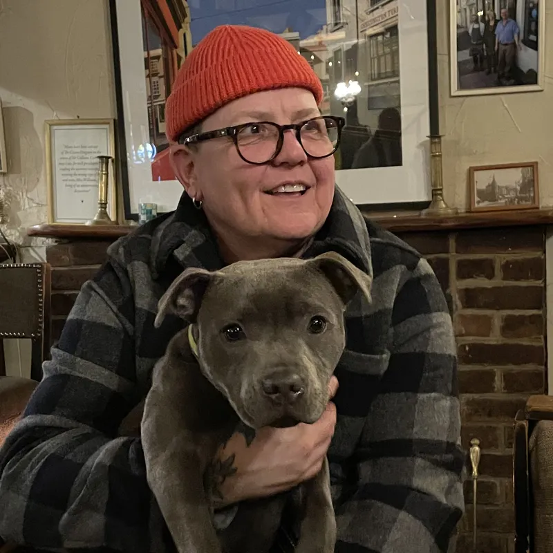 A person in a red beannie holding the cutest dog that ever lived.